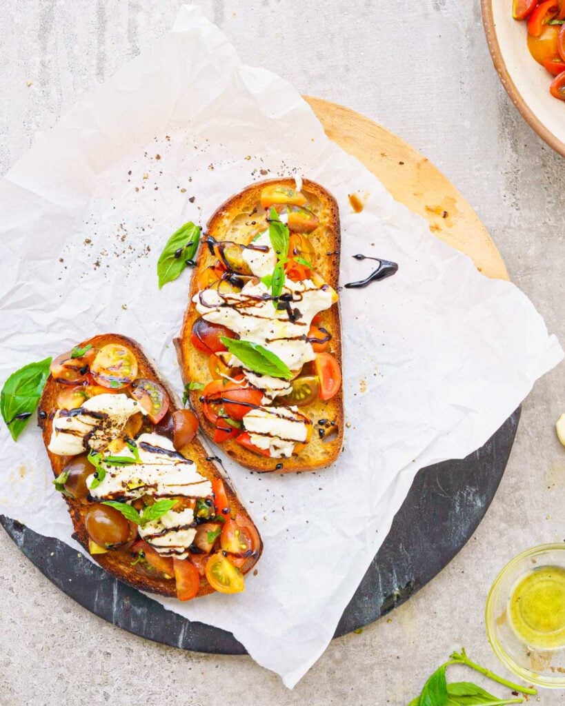 Burrata bruschetta-  Toasted bread on a baking paper, topped with slice cherry tomatoes, basil and burrata cheese with a drizzle of balsamic vinegar