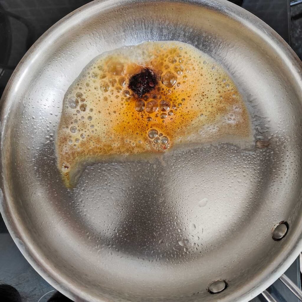 Stainless steel pan with chili crisp and butter that's bubbling.
