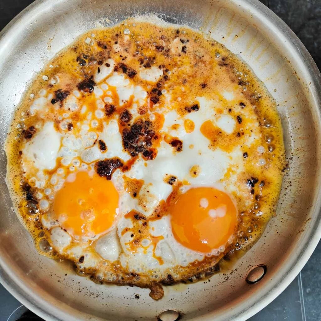 Two chili oil fried eggs in a skillet with chili oil on top.