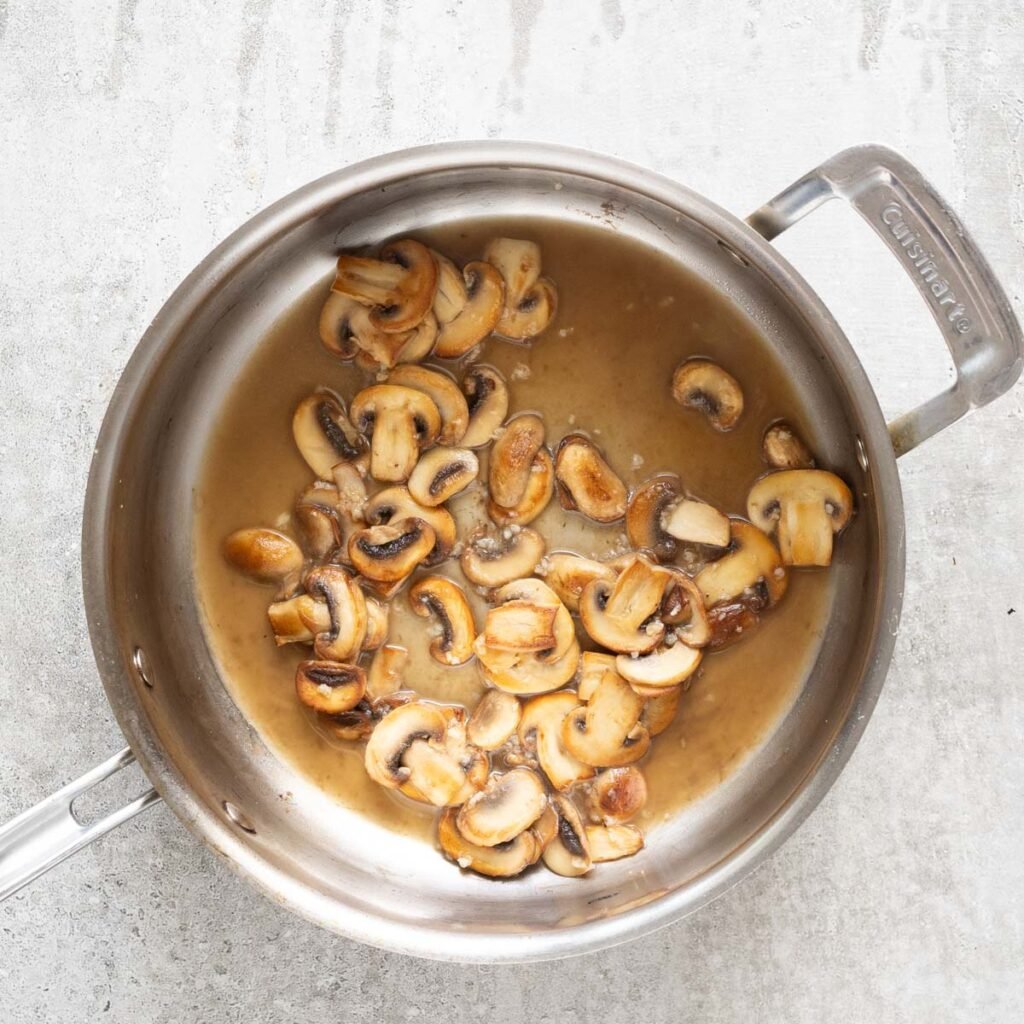 golden mushroom in a stainless steel pan with pasta water.