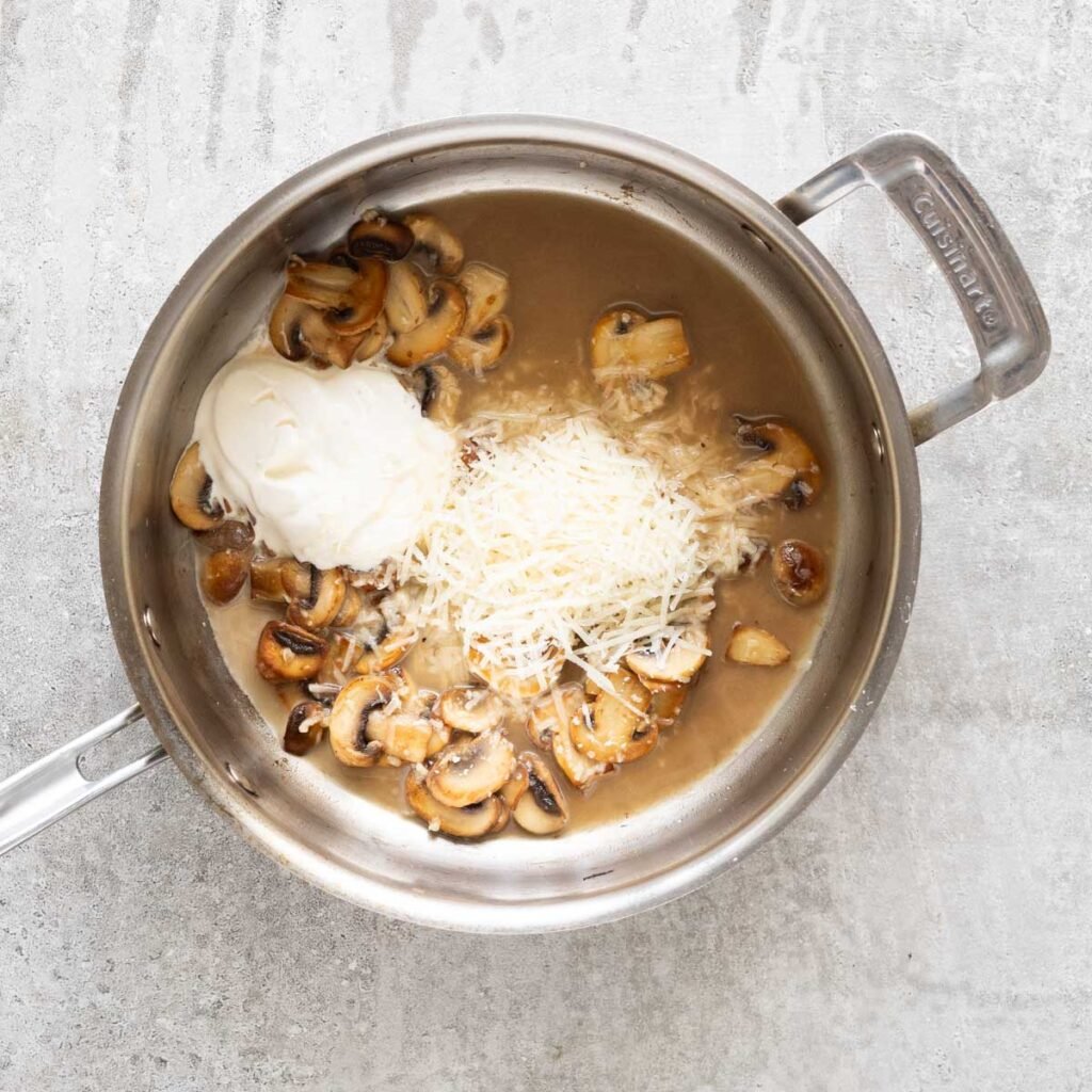 golden mushroom in a stainless steel pan with pasta water, cheese and cream.