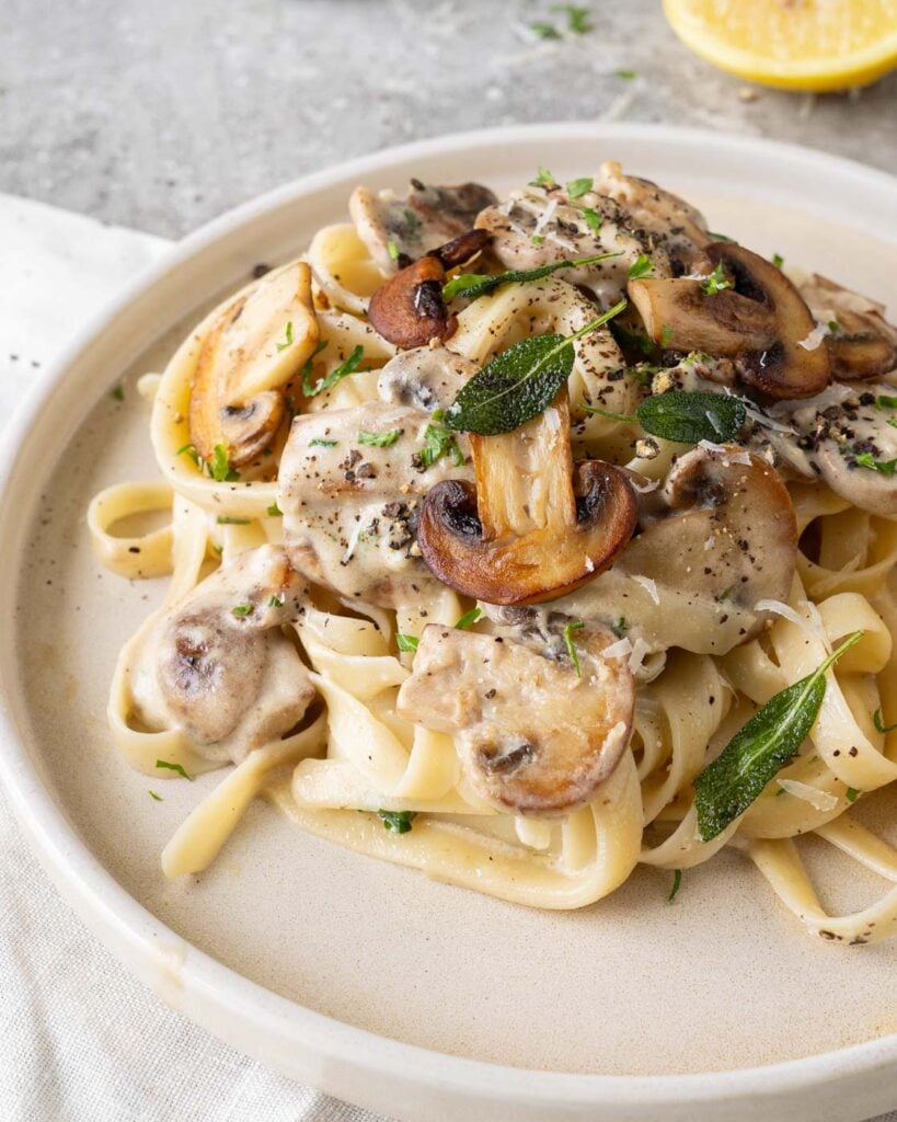 Truffle mushroom pasta on a beige plate, garnished with caramalized golden mushroom, crispy sage leaves.