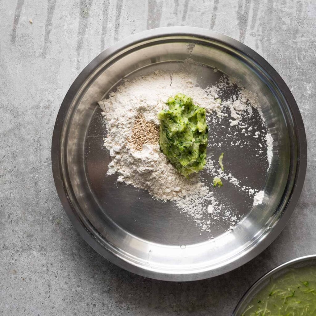 Grated zucchini, flour and sesame seeds in a big steel plate