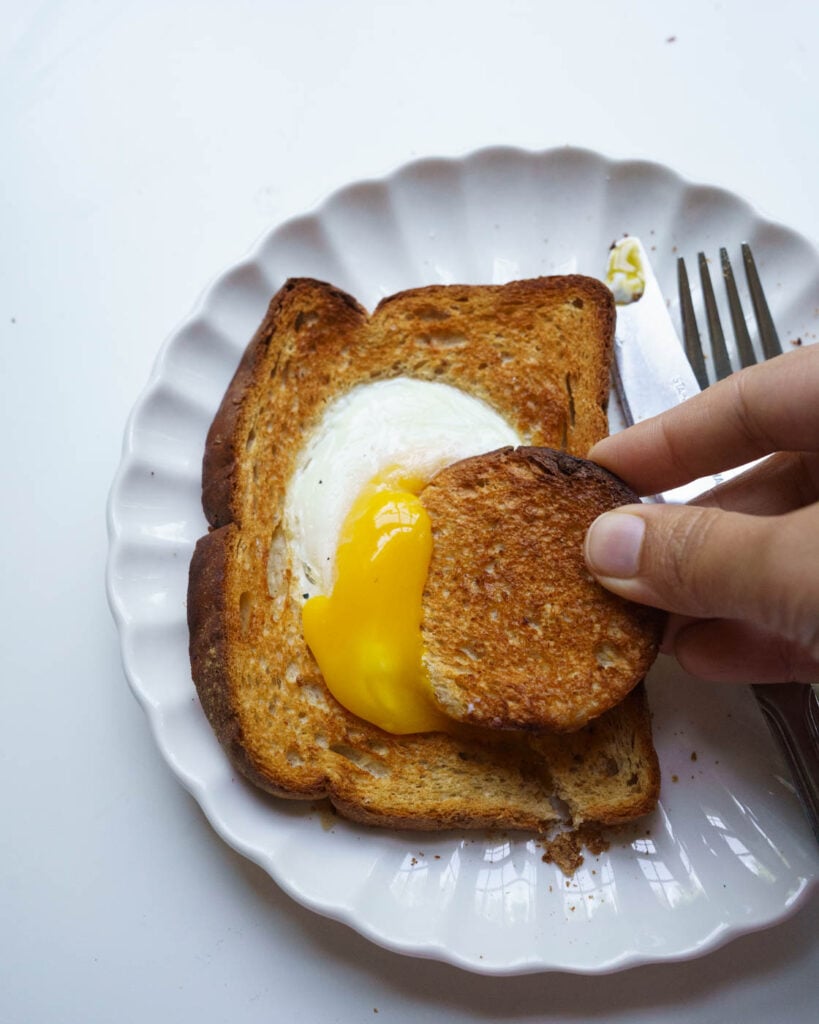 A toast with egg in the hole in the center on a white background.With a round toast piece breaking the egg yolk