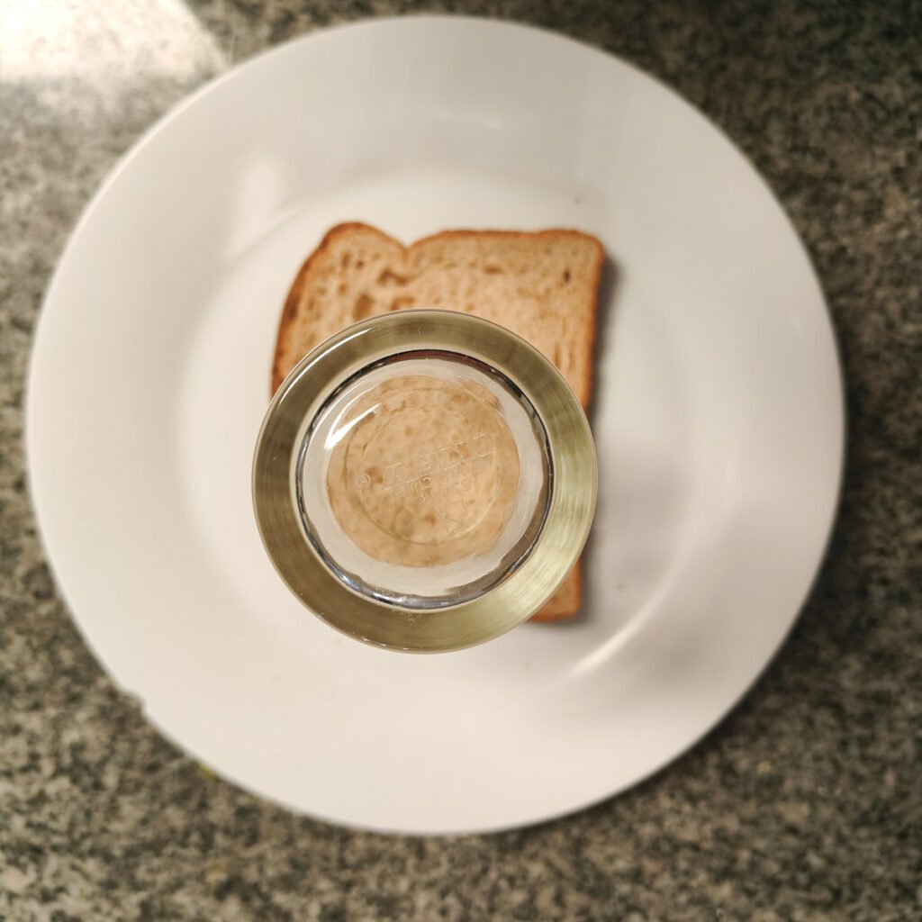 Bread on a white plate with a drinking glass on it.